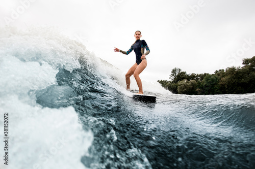 woman in wetsuit rides on wakesurf down on huge splashing river wave
