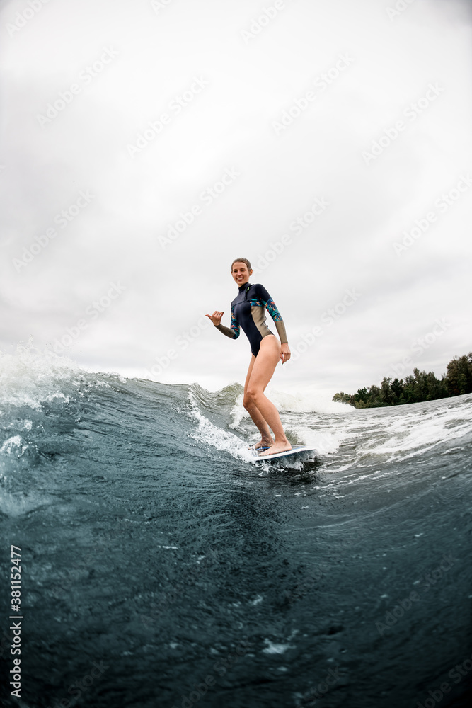 happy young athletic woman riding the river wave and showing hand gesture