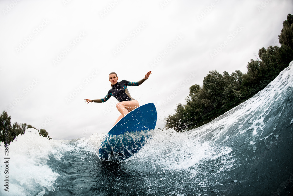 young woman stands with bent knees on surfboard and balanced on wave