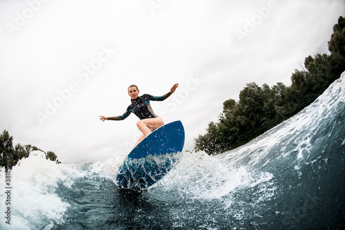 young woman stands with bent knees on surfboard and balanced on wave