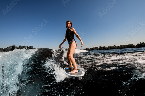 beautiful young athletic woman riding on the river wave and showing hand gesture