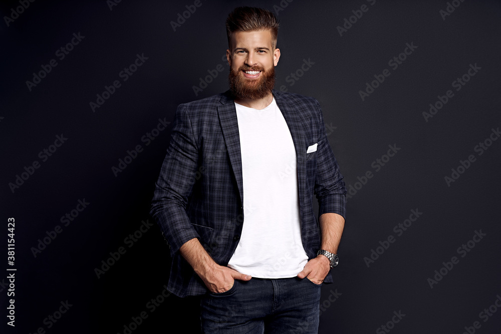 Confident and handsome. Young man with ginger beard in smart-casual clothes smiling looking at camera while posing against black background