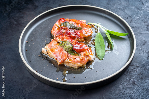 Modern style traditional Italian fried pork saltimbocca alla Romana with Parma ham and sage leaves offered as close-up in a Nordic design plate