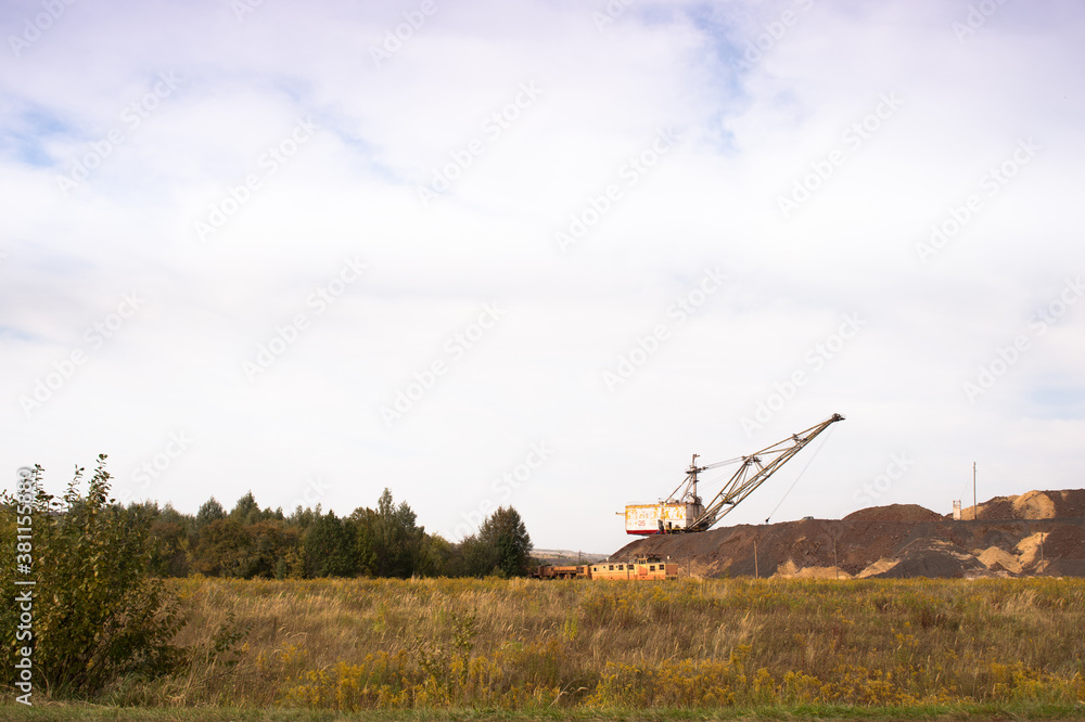 Fototapeta premium A large walking excavator forms dumps of rock delivered by freight train from a mining quarry. Background