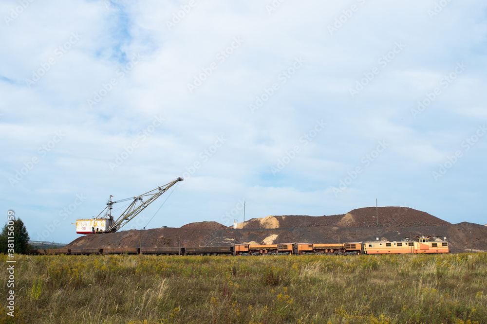 Fototapeta premium A large walking excavator forms dumps of rock delivered by freight train from a mining quarry. Background