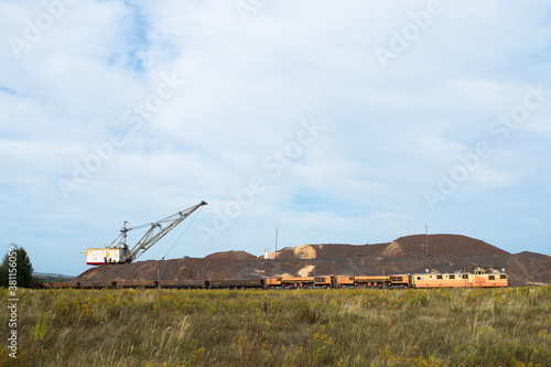 A large walking excavator forms dumps of rock delivered by freight train from a mining quarry. Background © Roman