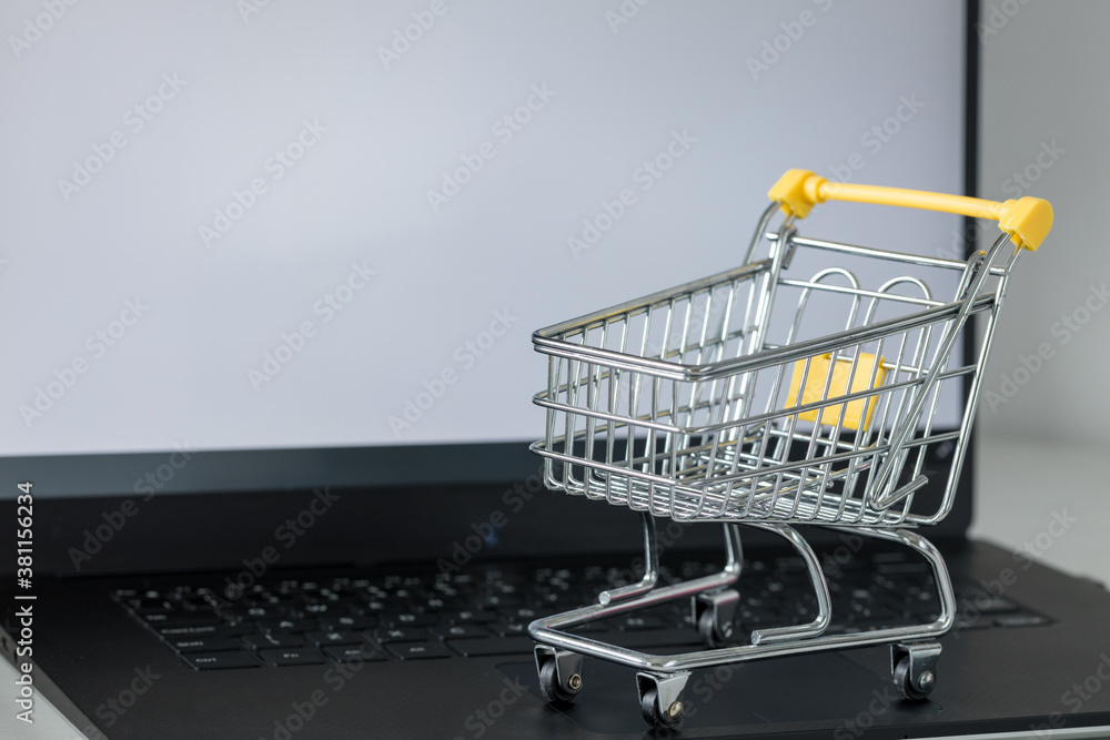 shopping cart on laptop keyboard. White monitor screen with space for text. Concept of online shopping and online stores