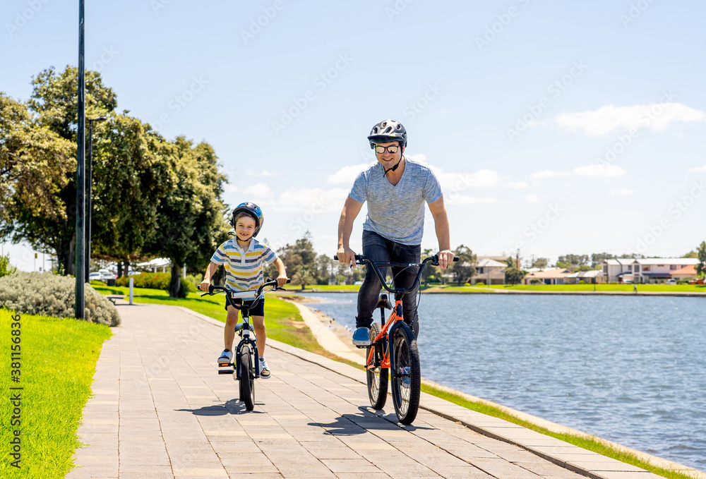 Obraz premium Father and son riding their bikes having fun together in the park by the lake