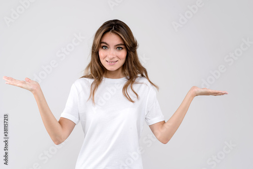 Atrractive young woman wearing white t-shirt isolated over white background showing confused expression with arms and hands raised. Doubt concept