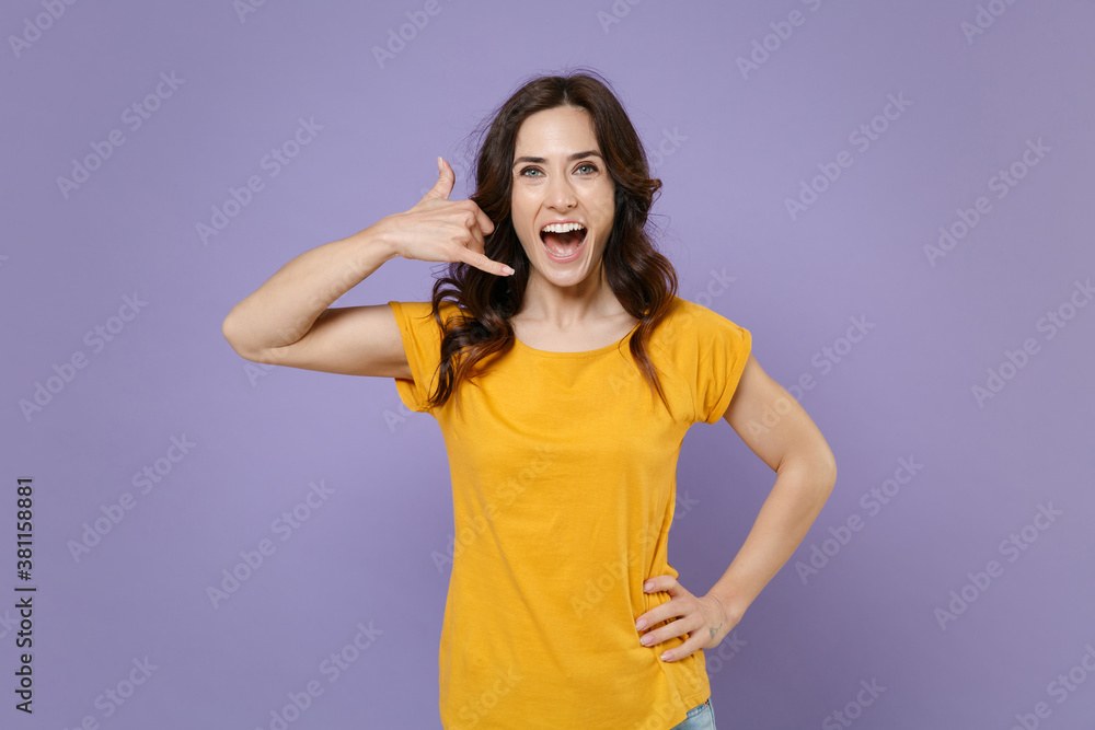 Excited cheerful funny young brunette woman 20s wearing basic yellow t-shirt doing phone gesture like says call me back looking camera isolated on pastel violet colour background, studio portrait. Excited cheerful funny young brunette woman 20s wearing basic yellow t-shirt doing phone gesture like says call me back looking camera isolated on pastel violet colour background, studio portrait.