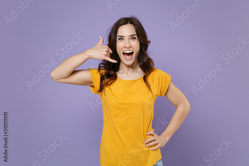Excited cheerful funny young brunette woman 20s wearing basic yellow t-shirt doing phone gesture like says call me back looking camera isolated on pastel violet colour background, studio portrait.