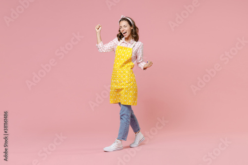 Papier peint Full length portrait joyful young woman housewife 20s in yellow apron doing winner gesture clenching fists keeping eyes closed isolated on pastel pink colour background studio