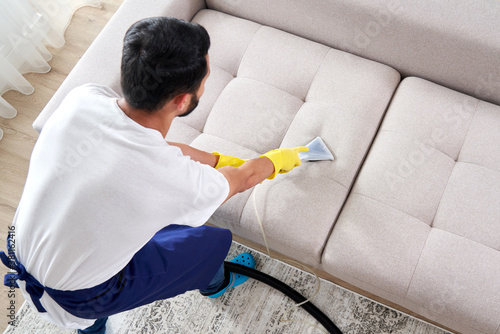 Close-up of housekeeper holding modern washing vacuum cleaner and cleaning dirty sofa with professionally detergent. Professional springclean at home concept photo