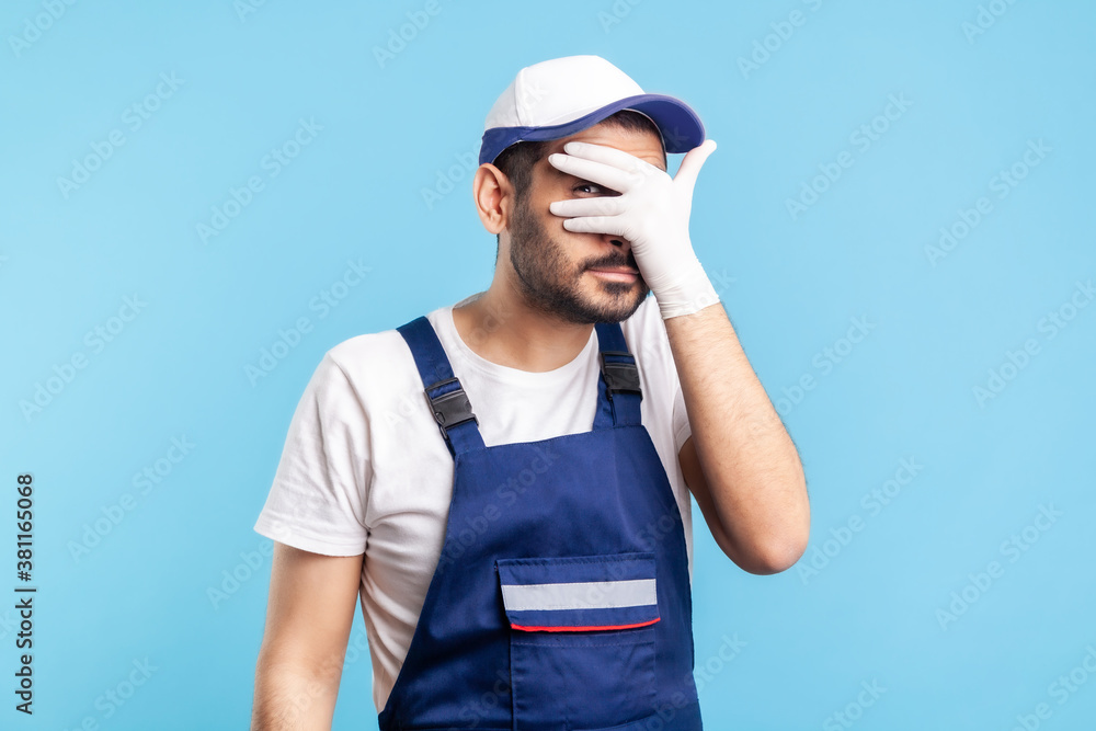 Curious, suspicious handyman in overalls and hygiene gloves looking through fingers, spying secret. Profession of service industry, courier delivery, housekeeping maintenance. studio shot isolated Curious, suspicious handyman in overalls and hygiene gloves looking through fingers, spying secret. Profession of service industry, courier delivery, housekeeping maintenance. studio shot isolated