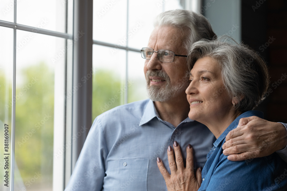 Smiling senior man and woman hug look in window distance thinking dreaming of happy future together. Dreamy mature Caucasian couple embrace imagine visualize healthy life. Elderly insurance concept. Smiling senior man and woman hug look in window distance thinking dreaming of happy future together. Dreamy mature Caucasian couple embrace imagine visualize healthy life. Elderly insurance concept.
