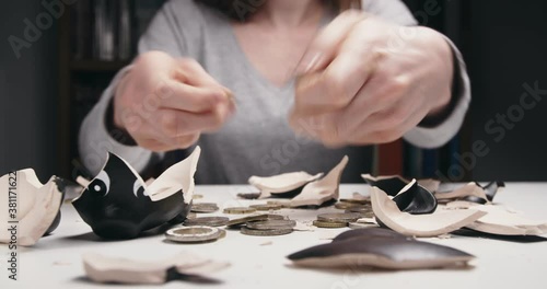 A Caucasian woman collecting coins from a broken piggy bank.