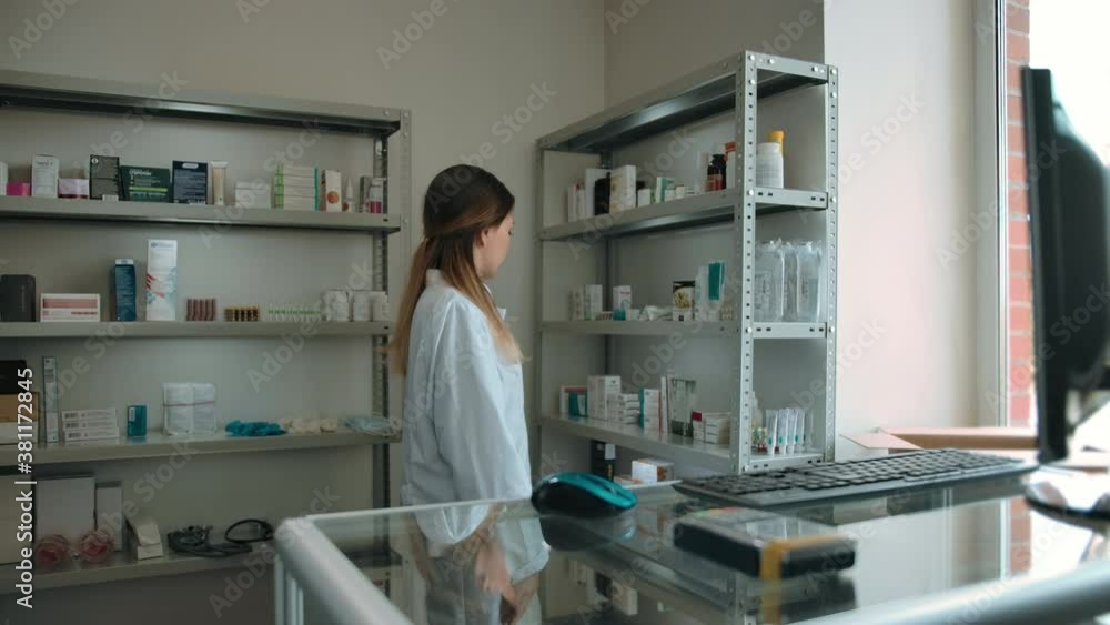 Dolly in shot on the pharmacist girl in the interior of the pharmacy. A beautiful young woman pharmacist in a white robe looks at the camera and smiles. Checking goods on the shelves. Dolly in shot on the pharmacist girl in the interior of the pharmacy. A beautiful young woman pharmacist in a white robe looks at the camera and smiles. Checking goods on the shelves.