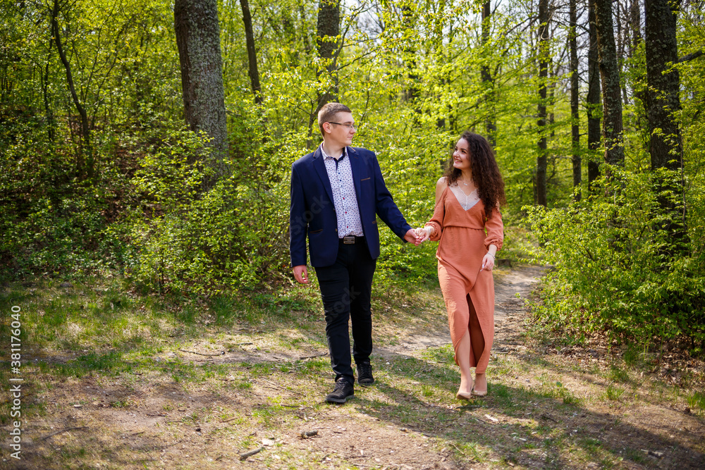 Fototapeta premium Beautiful couple in the woods. Girl with elegant haircut hugs her man in a suit. Rustic outdoors details photography portrait. Happy woman and boyfriend