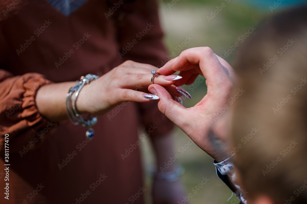 Fototapeta premium Image of a man putting a silver wedding ring on a woman's hand, outdoors. Sea or river background
