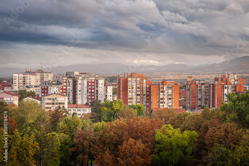 Autumn colors of foreground trees, doft light on old buildings and dramatic, blue hour sky above Pirot cityscape