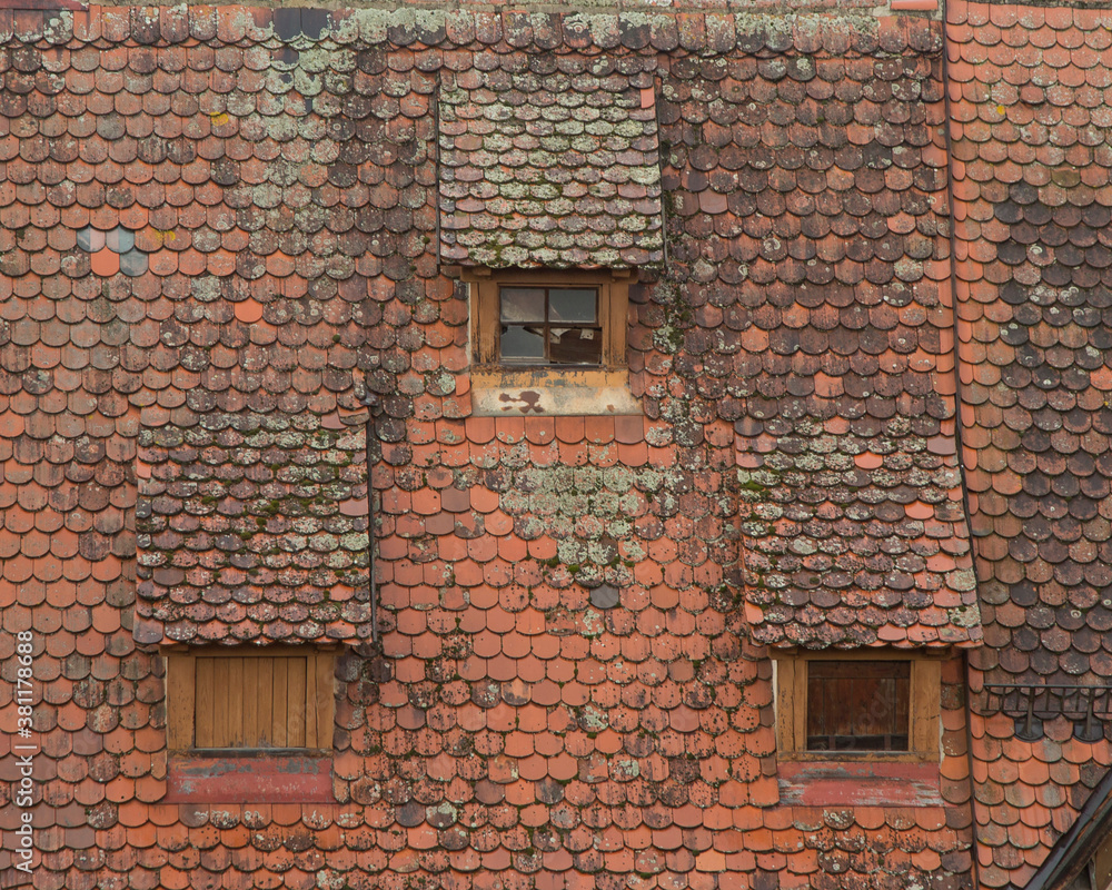 Horizontal picture of old roof with three little windows in Germany, Europe. Rooftop covered with red tiles with spots of lichen