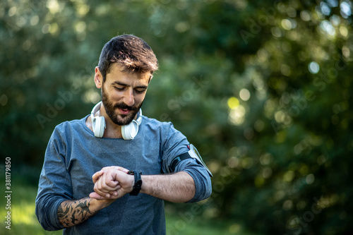 A young man stands in nature and looks at his smart watch on a sunny day photo