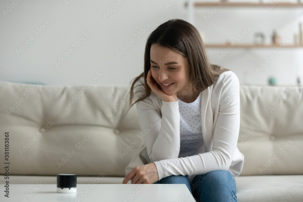 Happy millennial Caucasian girl look at modern smart wireless speaker playing good quality music. Smiling young woman client or buyer relax at home listen to music using mobile gadget or device. Happy millennial Caucasian girl look at modern smart wireless speaker playing good quality music. Smiling young woman client or buyer relax at home listen to music using mobile gadget or device.