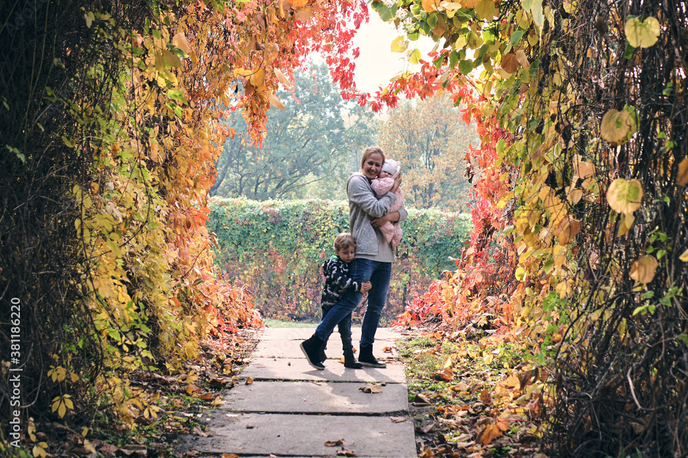 Autumn family walk in forest. Beautiful park with dry yellow and red leaves. Loving Mother hugs daughter and son Autumn family walk in forest. Beautiful park with dry yellow and red leaves. Loving Mother hugs daughter and son