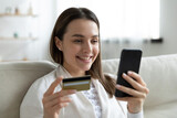 Overjoyed female client shopping online on smartphone from home with credit card. Happy young Caucasian woman make secure internet payment on cellphone, use banking application or service system.
