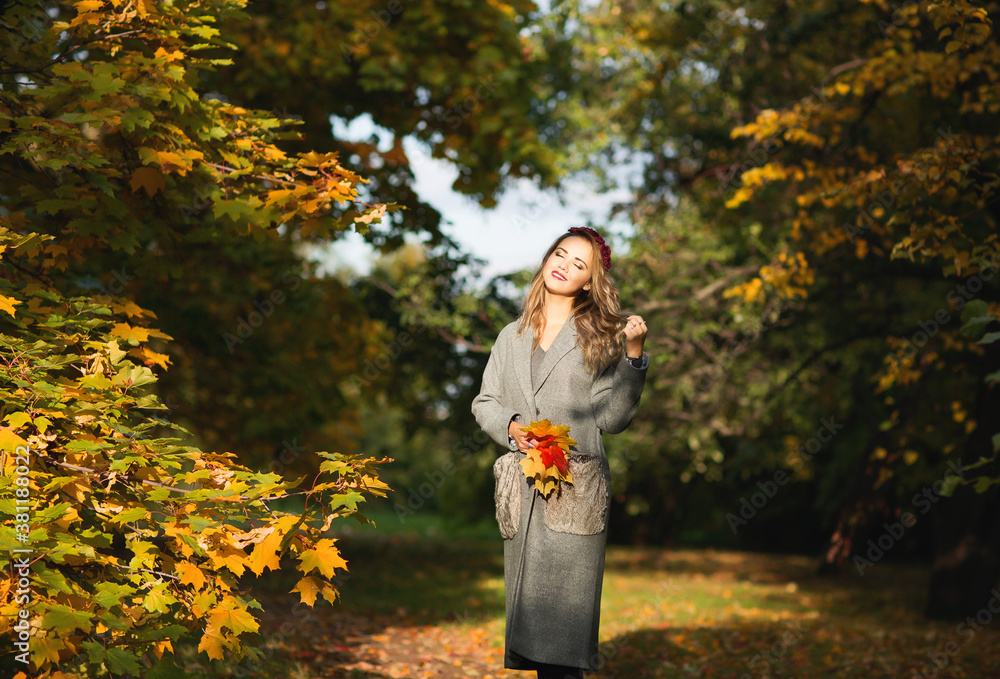 Outdoors lifestyle fashion portrait of beautiful young woman walking on the autumn park. Wearing stylish grey oversized coat with fur pockets. Smiling and enjoying autumn nature. Autumn colors Outdoors lifestyle fashion portrait of beautiful young woman walking on the autumn park. Wearing stylish grey oversized coat with fur pockets. Smiling and enjoying autumn nature. Autumn colors