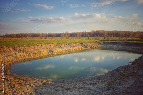 A small drying pond in the evening in the field. Cloudy sky over the lake. Landscape.