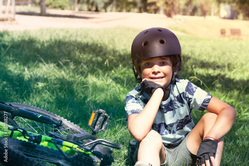 Portrait of a child with black helmet in summer park, resting after biking.