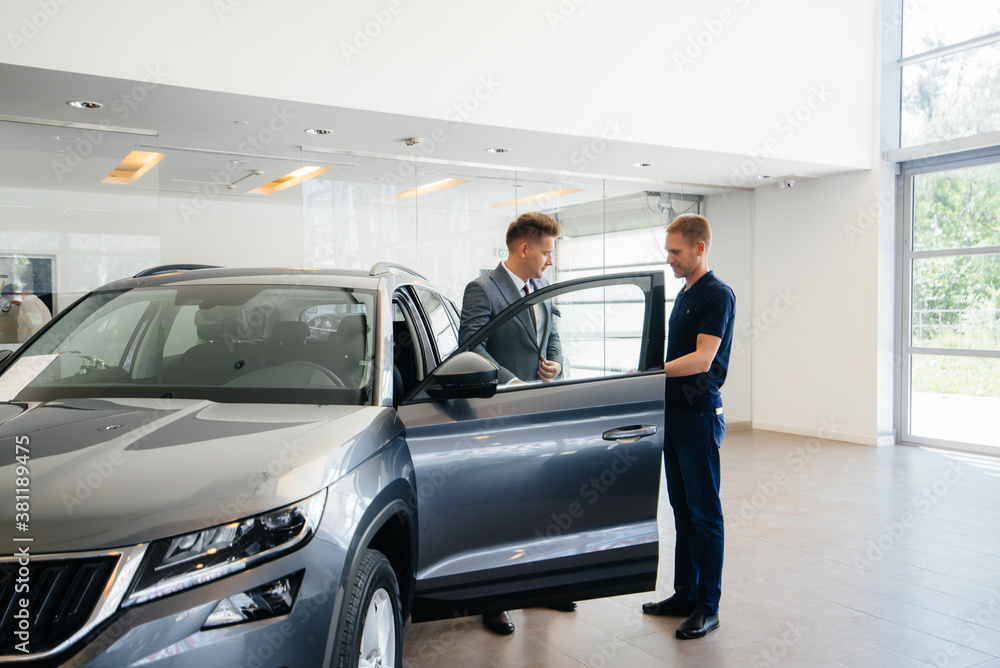 A young businessman with a salesman looks at a new car in a car dealership. Buying a car A young businessman with a salesman looks at a new car in a car dealership. Buying a car