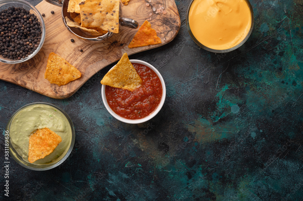 Top view of tortilla chips with different souses on dark background. Nachos with cheese dip, salsa and avocado sous. Food concept. Unhealthy meal. Mexican traditional taste.