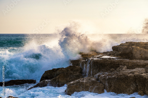 Große Welle prallt gegen den Felsen einer Küste im Sonnenlicht