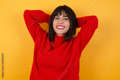 Caucasian brunette woman wearing red casual sweater isolated over yellow background stretching arms, relaxed position. © Roquillo