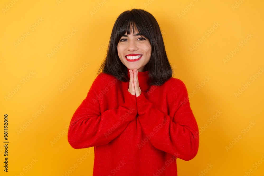 Caucasian brunette woman wearing red casual sweater isolated over yellow background praying with hands together asking for forgiveness smiling confident. Caucasian brunette woman wearing red casual sweater isolated over yellow background praying with hands together asking for forgiveness smiling confident.
