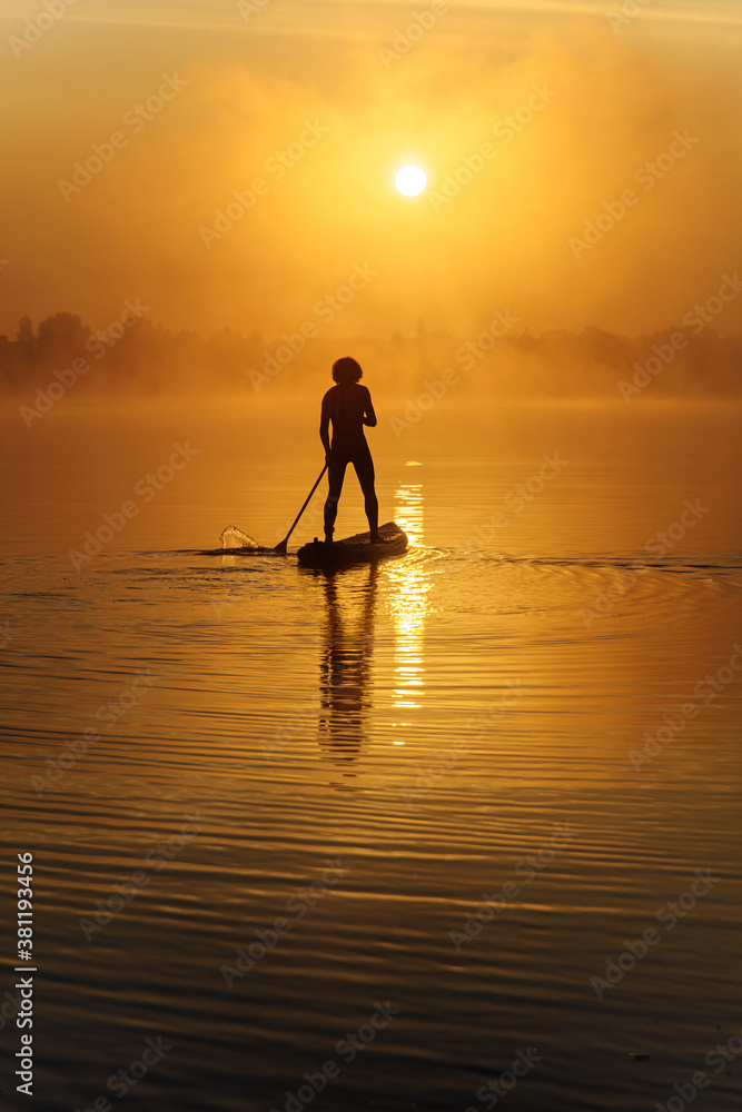 Back view of healthy man rowing with paddle board on lake