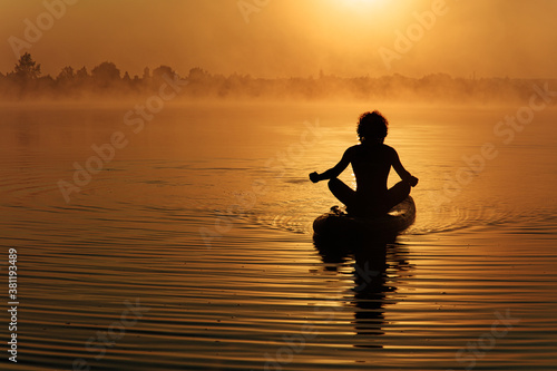 Muscular man meditating on paddle board during sunrise