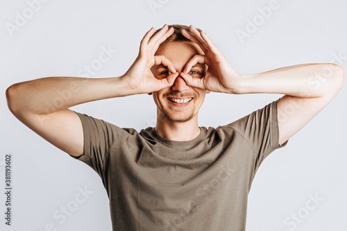 Young handsome brunet man with beard says ok and winks on white isolated background