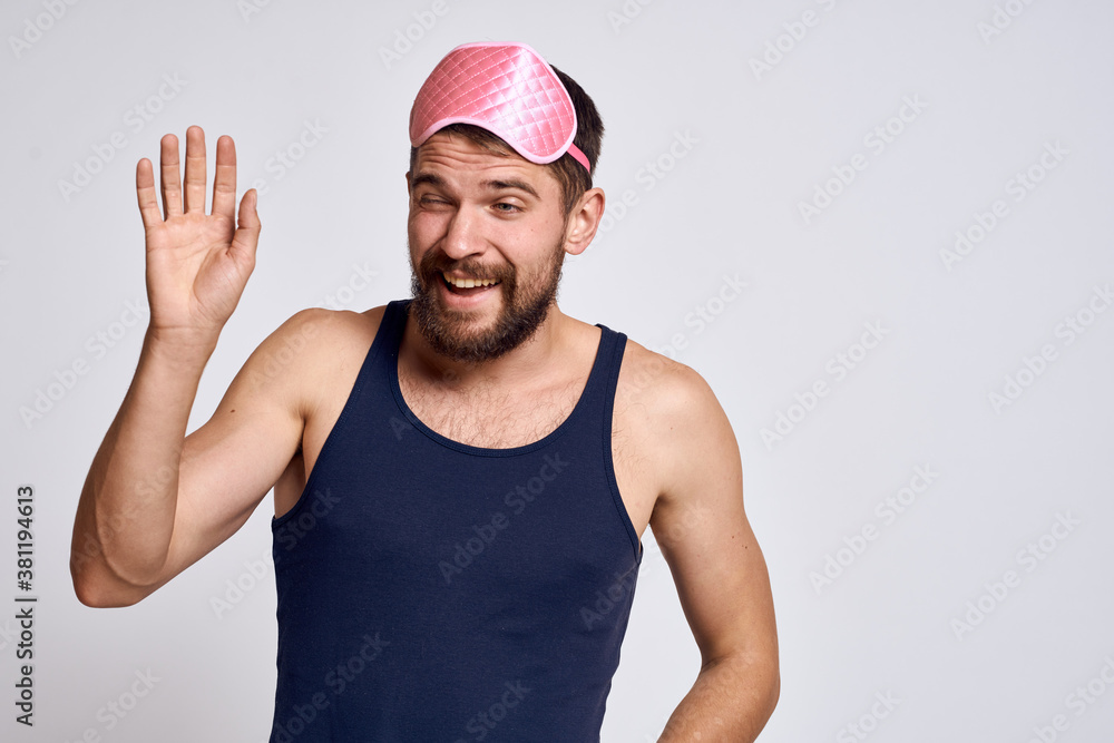 A man with a pink sleep mask AND a black T-shirt on a gray background cropped view
