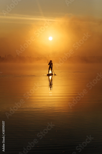 Young man practising in sup surfing during amazing sunrise