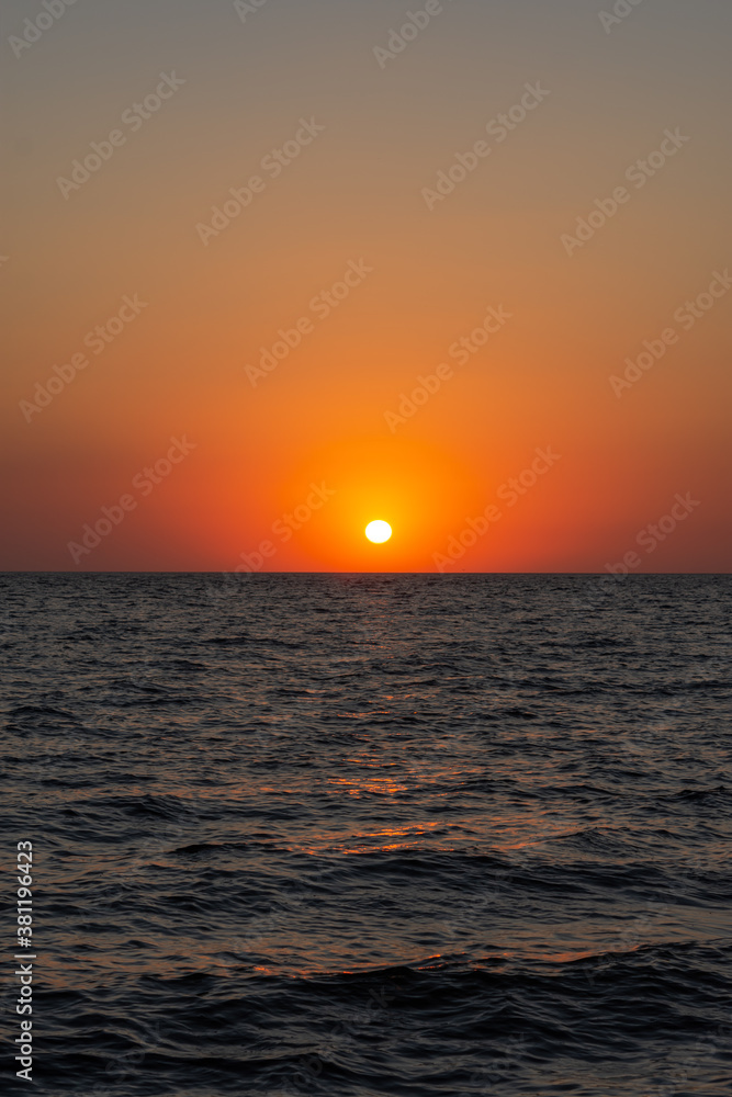 Beautiful orange sunset over the sea. The sun is sinking below the horizon. Relaxing sea landscape. The scarlet hues of the sky and sea water. Sunset over the Black sea. Natural background.