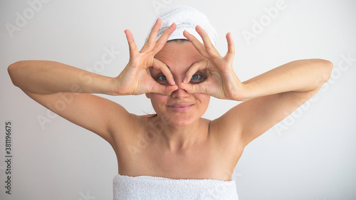 Woman in bath towel holding fingers near eyes like glasses: mask like super hero or owl