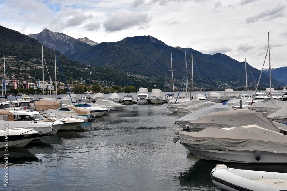 Sailing yachts arranged in rows in a marina covered for winter season and with lowered sails. The vessels anchor on Lake Maggiore in Locarno in Switzerland.