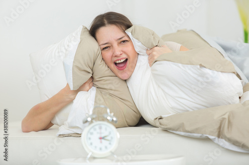 Obraz na plátně young woman holding pillows over ears to drown out alarm