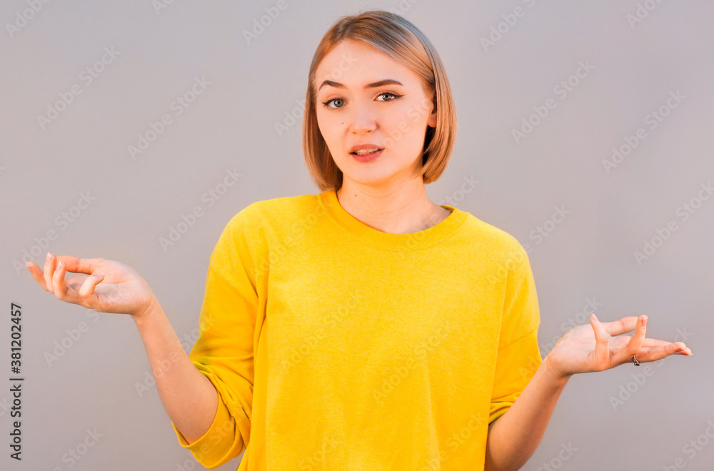 Portrait of a young woman shrugging shoulders over gray background Portrait of a young woman shrugging shoulders over gray background