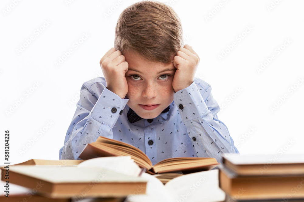 The schoolboy is bored at the table with books. Education and training. White background. The schoolboy is bored at the table with books. Education and training. White background.