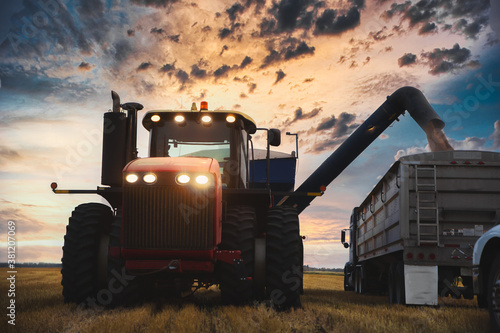 A tractor with a grain cart unloading wheat into a semi trailer in a agricultural autumn landscape
