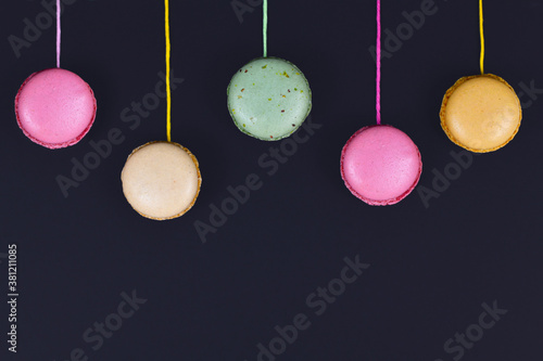 Colorful French macaron attached to strings hanging from top of black background with empty copy space photo